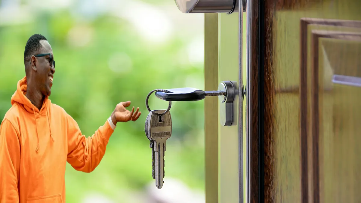 Black man wearing an orange sweater happily pointing to his house key